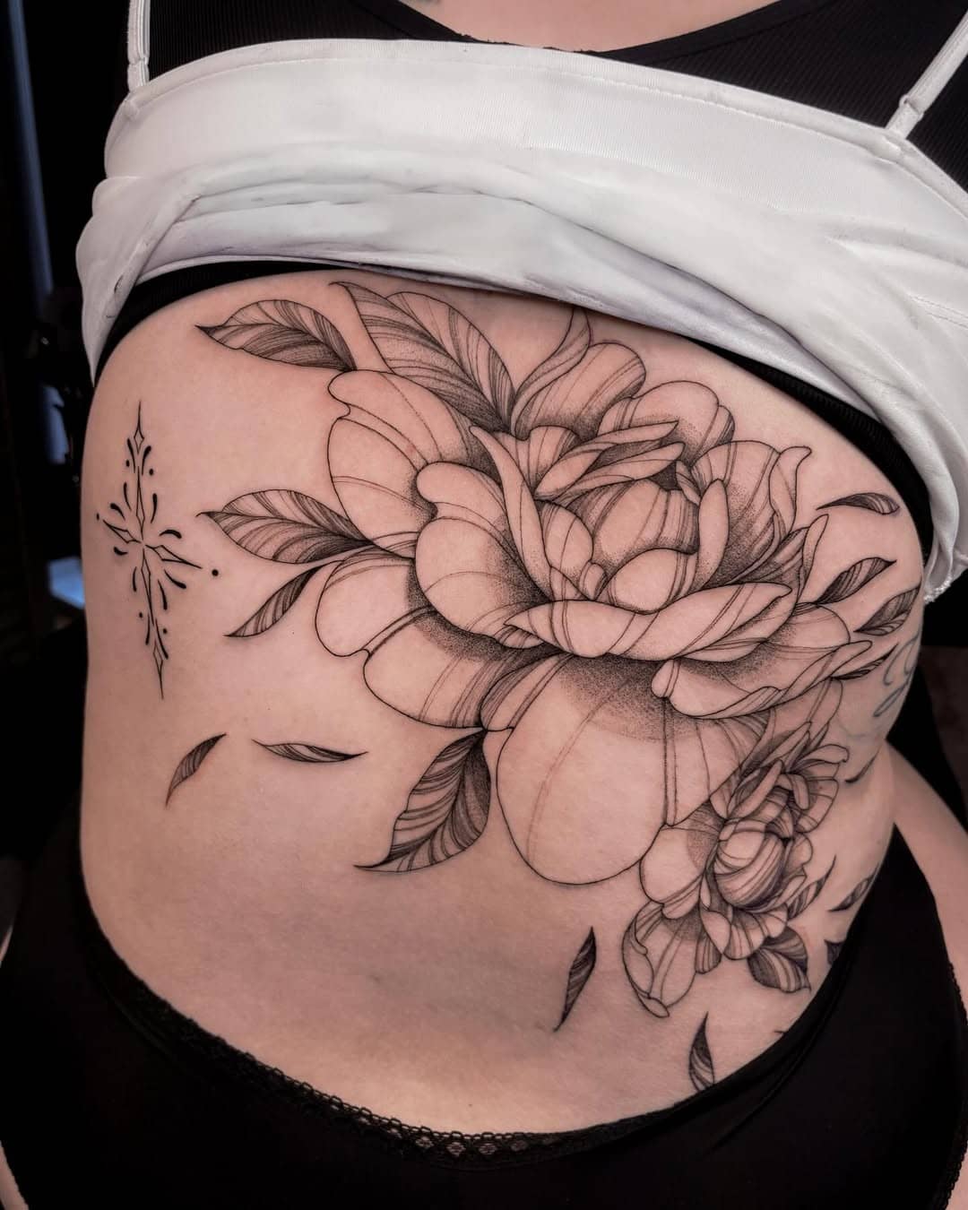 Tatuaż w stylu fineline – duży kwiat z liśćmi na boku ciała, Nava w Sztorm Tattoo Gdańsk