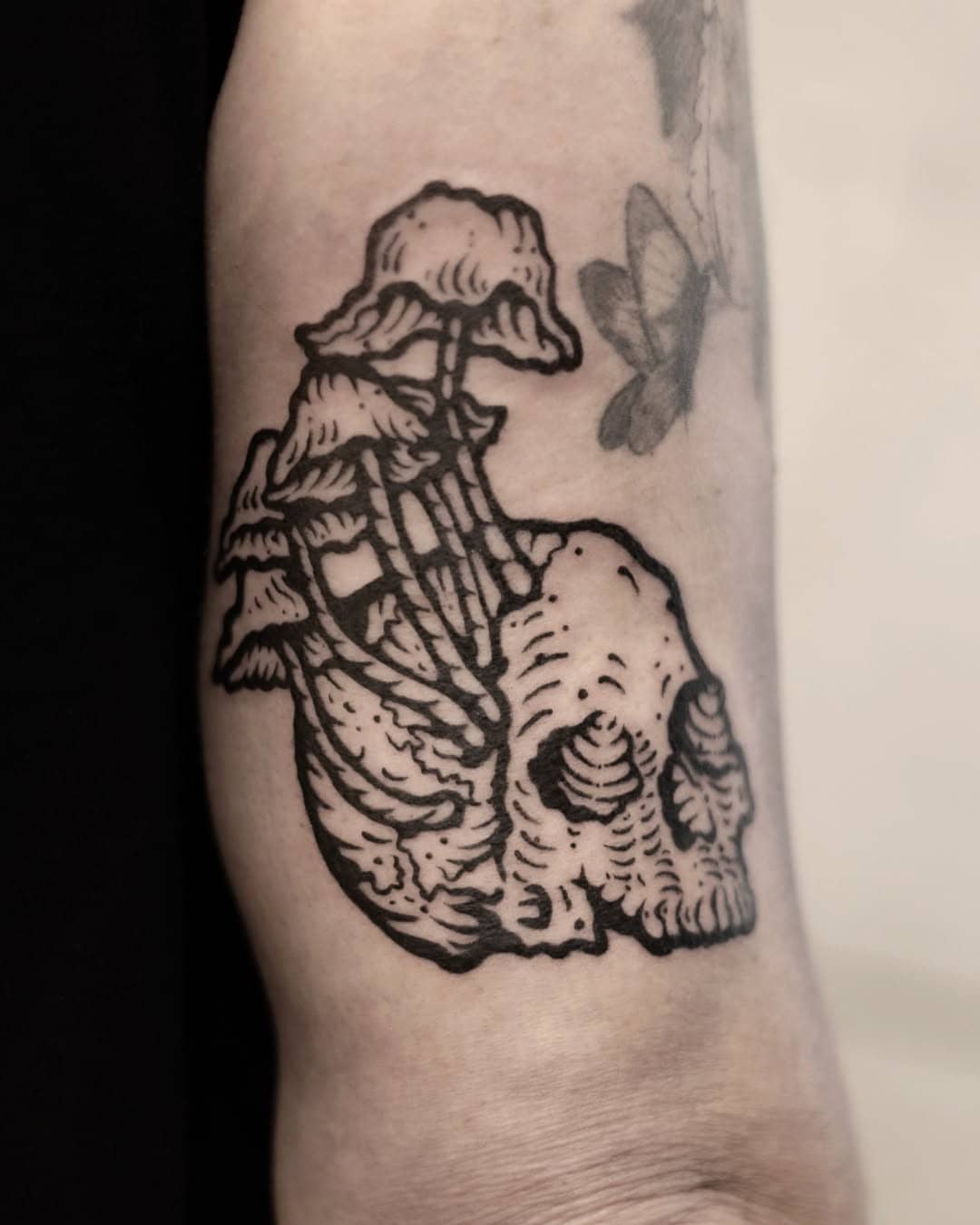 Tatuaż w stylu linework przedstawiający czaszkę, z której wyrastają grzyby. Mocny kontrast, graficzna kreska i mroczny klimat. Projekt Oriany, Sztorm Tattoo Gdańsk.