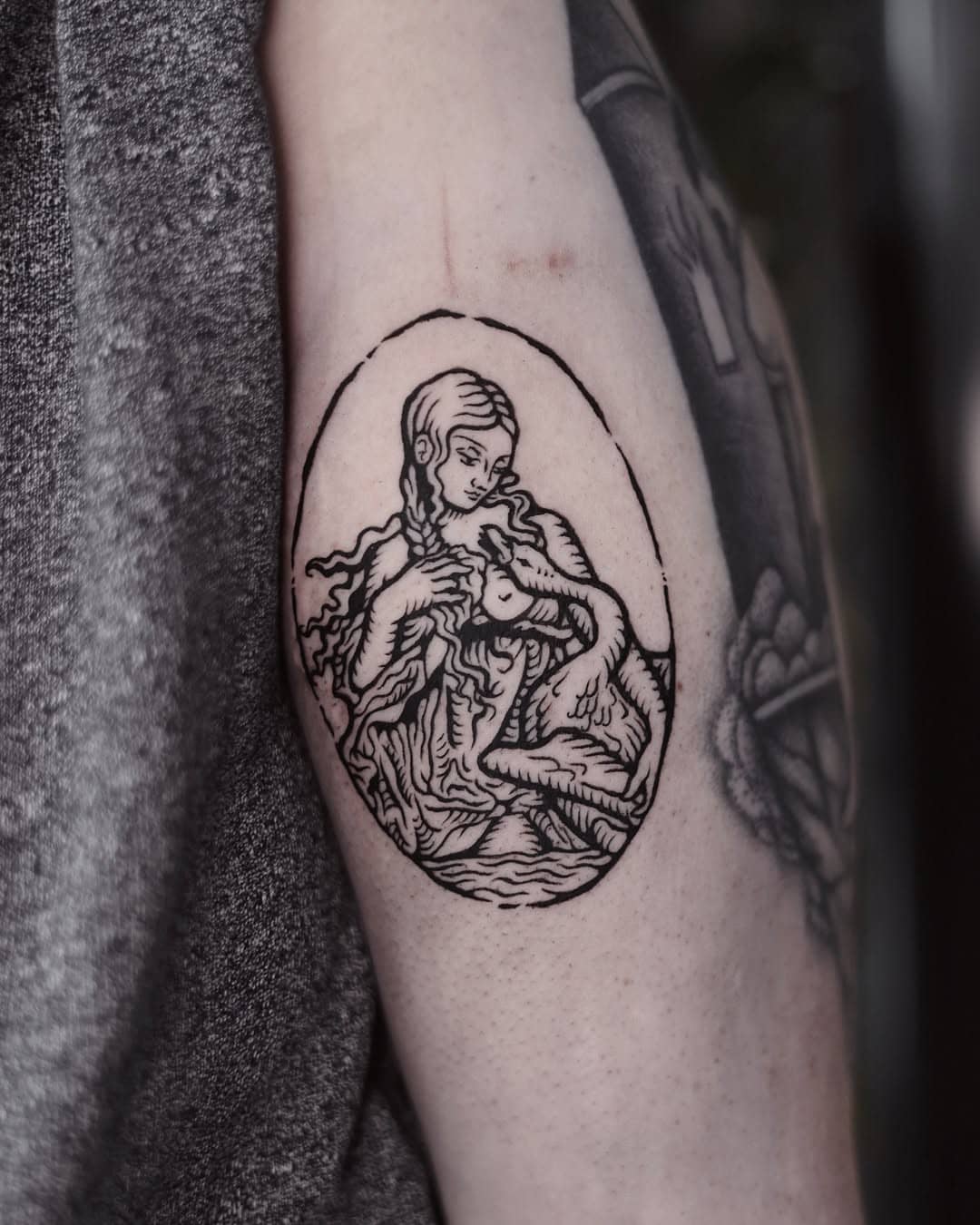 Ornamentowy tatuaż w stylu linorytowym przedstawiający Madonnę z dzieckiem w owalu, wykonany na ramieniu w Sztorm Tattoo Gdańsk.