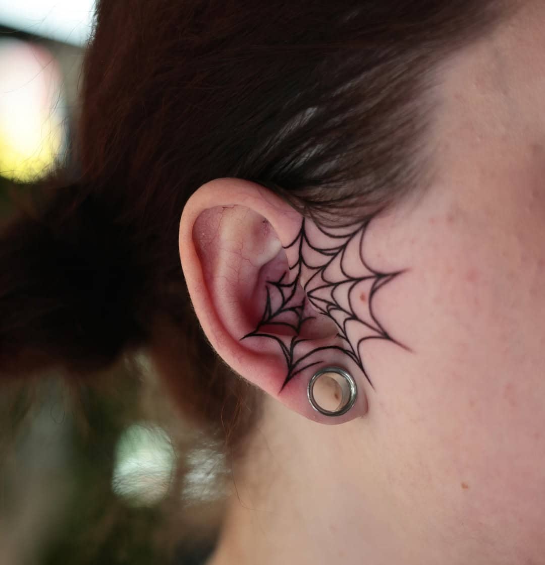 Tatuaż pajęczyna na uchu, czarne cienkie linie w stylu graficznym. Studio Sztorm Tattoo Gdańsk.