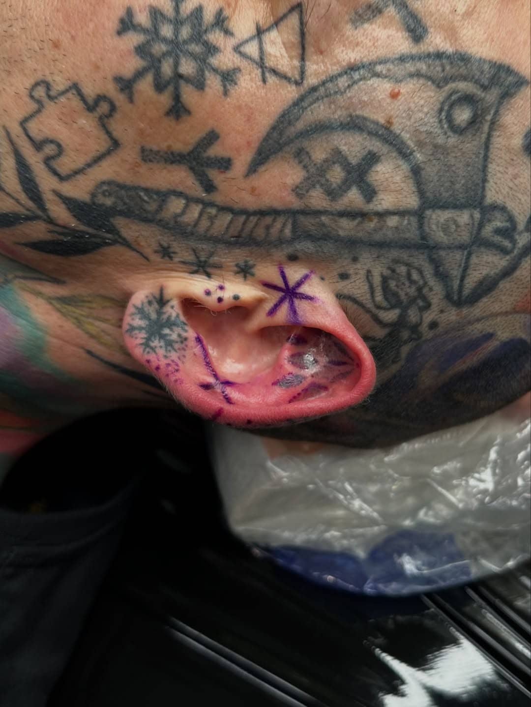 Tatuaż w uchu z motywami gwiazdek i śnieżynek, wkomponowany w istniejące tatuaże na głowie. Studio Sztorm Tattoo Gdańsk.