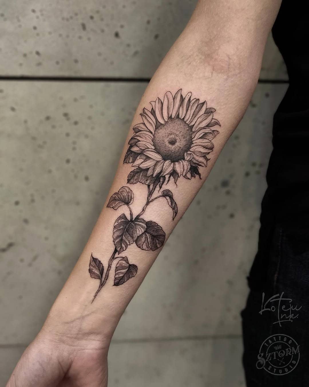 Delikatny tatuaż słonecznika na przedramieniu, utrzymany w linearnym i graficznym stylu. Praca Oli.