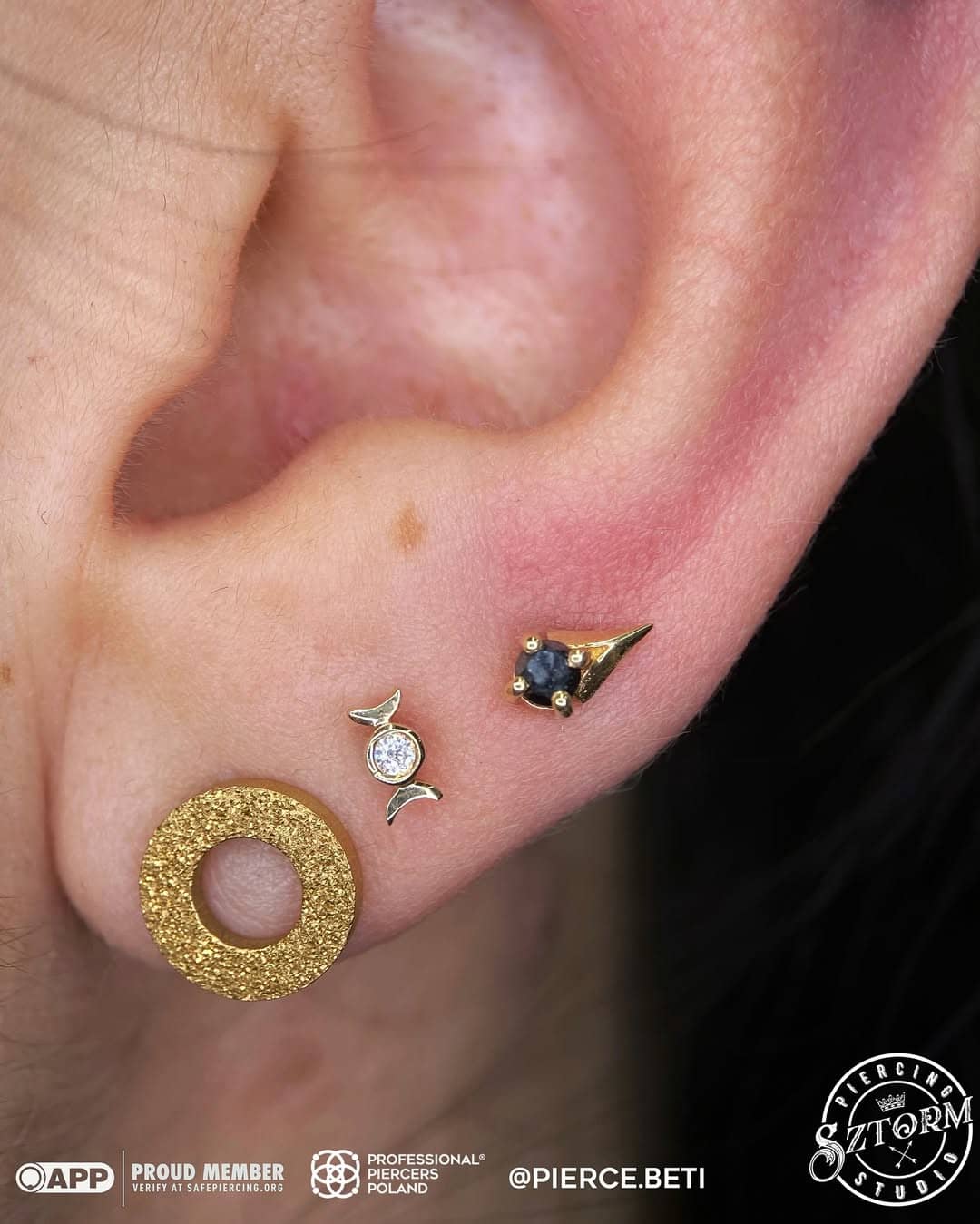 Biżuteria do piercingu ucha – złoty trójkąt z cyrkoniami i srebrny kolczyk z kryształem, Sztorm Tattoo Gdańsk.