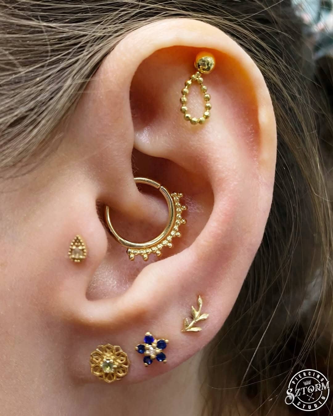 Złote kolczyki do piercingu ucha w kształcie koła i kwiatu, Sztorm Tattoo Gdańsk.